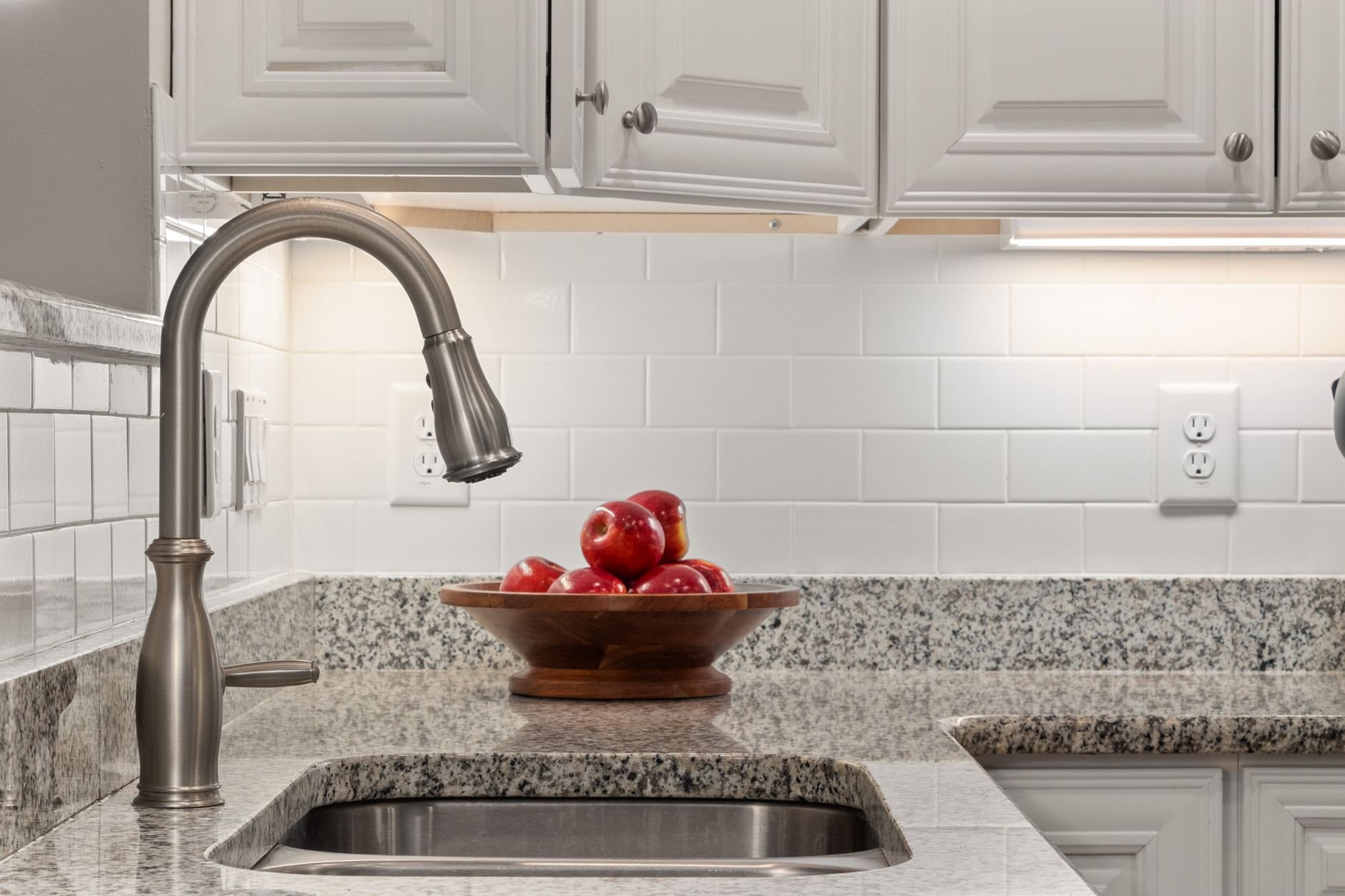 Elegant kitchen countertop featuring fresh apples in a wooden bowl beside a sleek stainless steel sink.